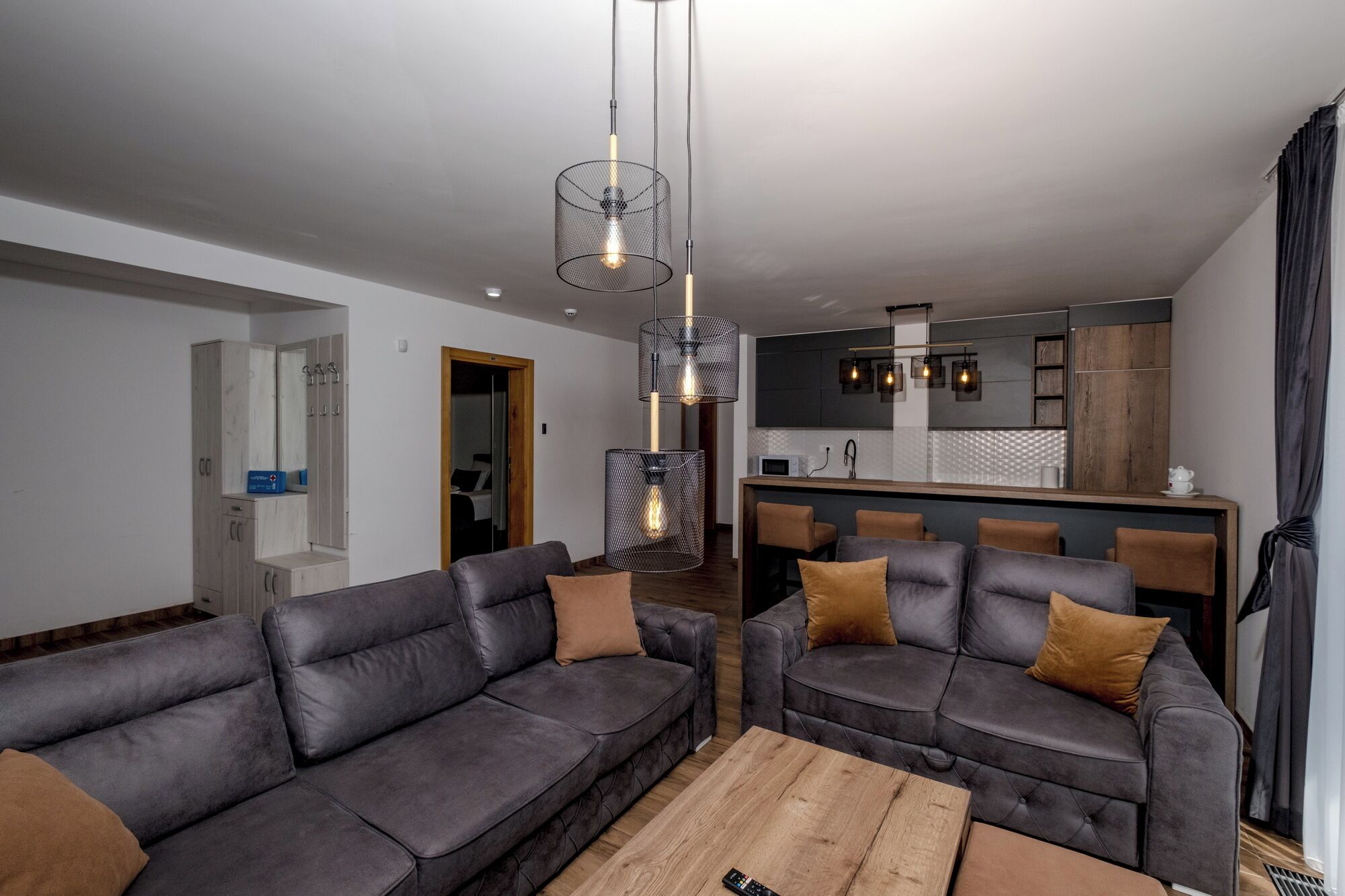 A modern living room with a grey sectional sofa, a wooden coffee table, and a kitchen area in the background.