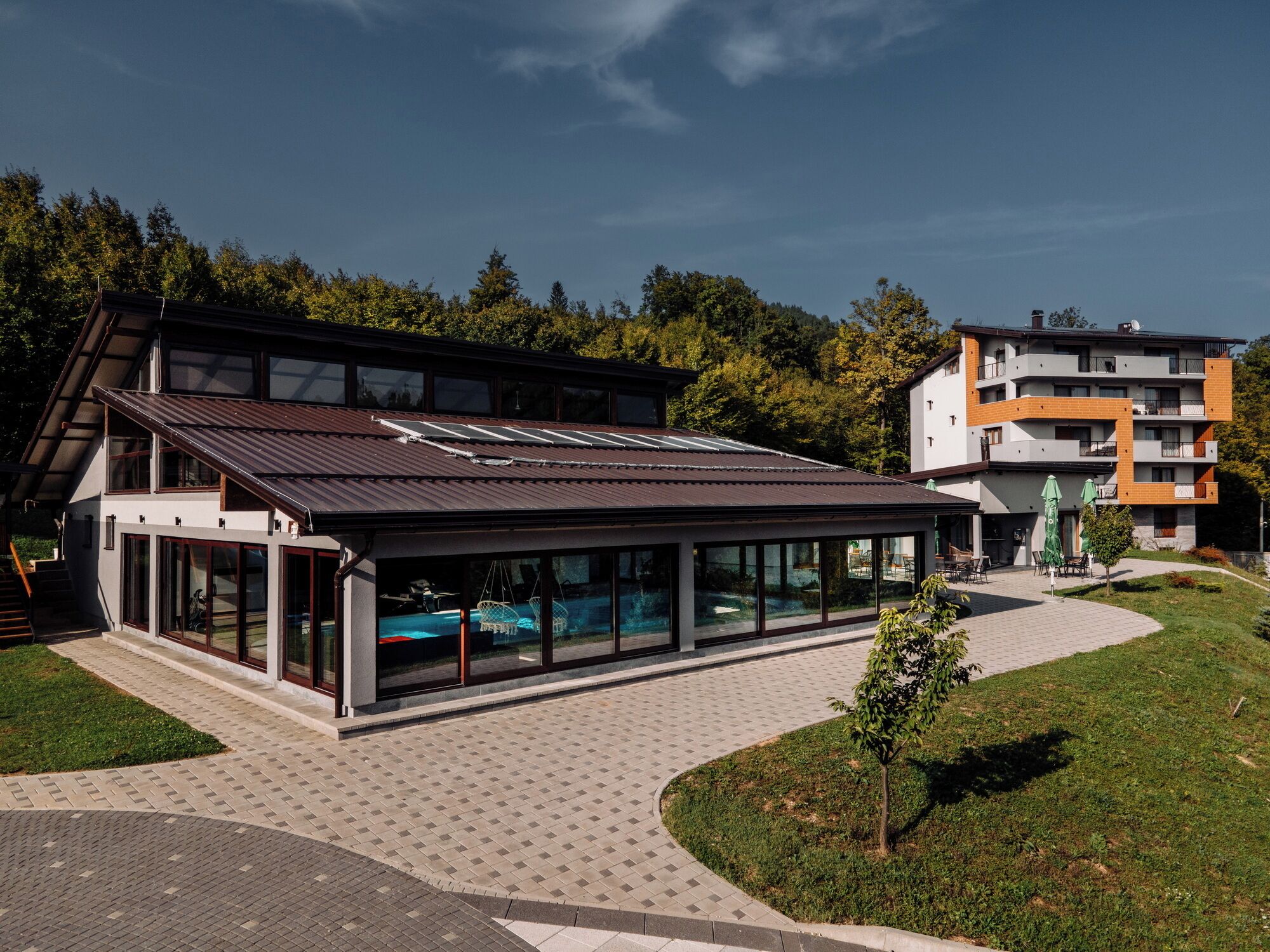 A modern building with a large glass facade, a covered outdoor area, and a swimming pool.