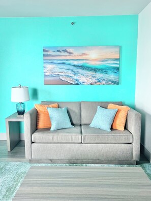 Ein Wohnzimmer mit grauem Sofa, türkisblauen Wänden und einem Meeresbild.