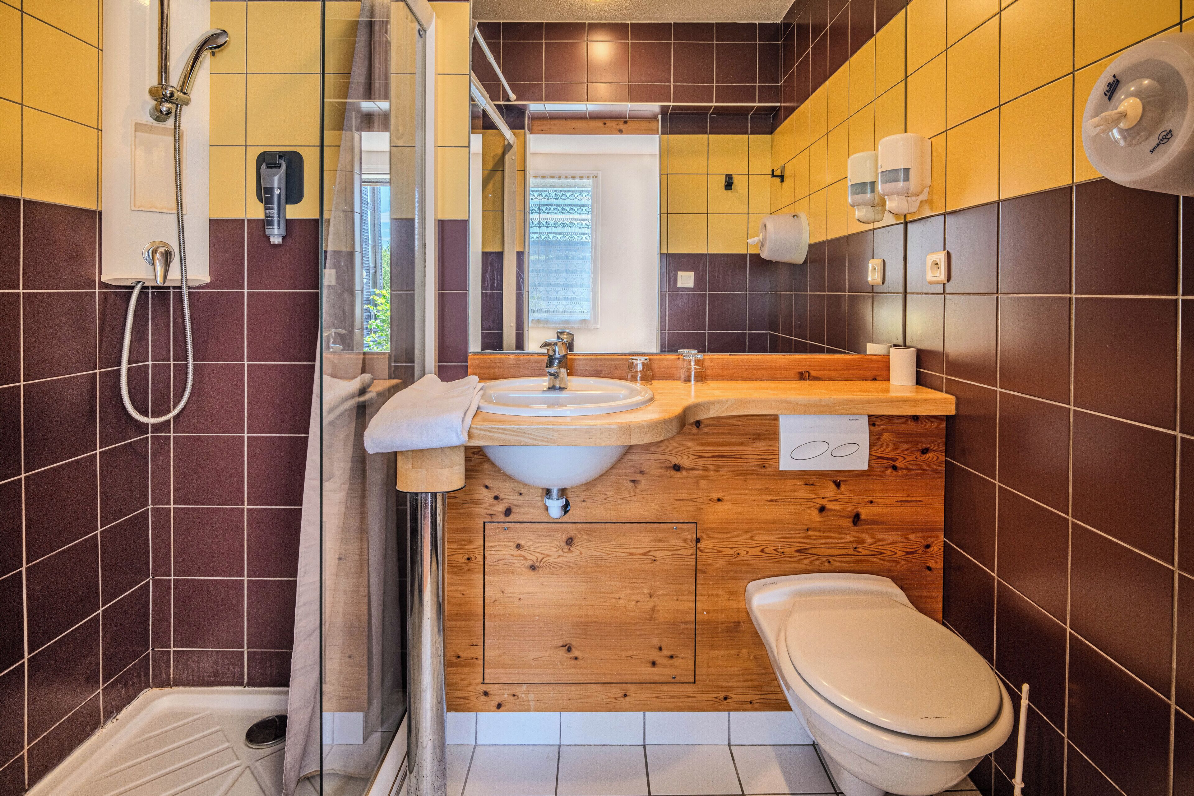 A modern bathroom with a shower, sink, and toilet, featuring wooden paneling and tiled walls.