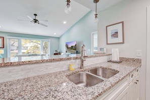 A kitchen with granite countertops, stainless steel sinks, a ceiling fan, and a framed picture on the wall. - Lagoon-View Villa Steps from the Beach (Isle of Palms)