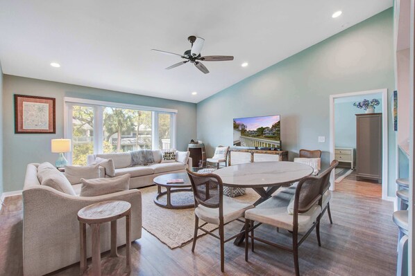 A spacious living area with a sofa, coffee table, and dining table, a ceiling fan, and a TV. - Lagoon-View Villa Steps from the Beach (Isle of Palms)