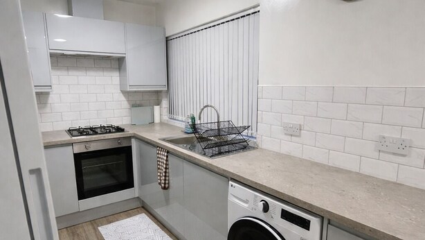 Uma cozinha moderna com armários brancos, forno embutido, máquina de lavar roupa e um relógio na parede.