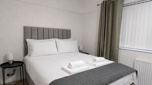 Quarto moderno com cama, mesa de cabeceira e janela com cortinas.