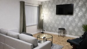 Uma sala de estar moderna com um sofá, uma mesa de centro redonda, uma TV de tela plana na parede e um piso estampado.
