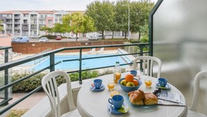 A balcony with a table set for breakfast, a pool view, and a building with balconies in the background. - Proche du port | Balcon privé & vue sur le port (Les Sables d'Olonne)