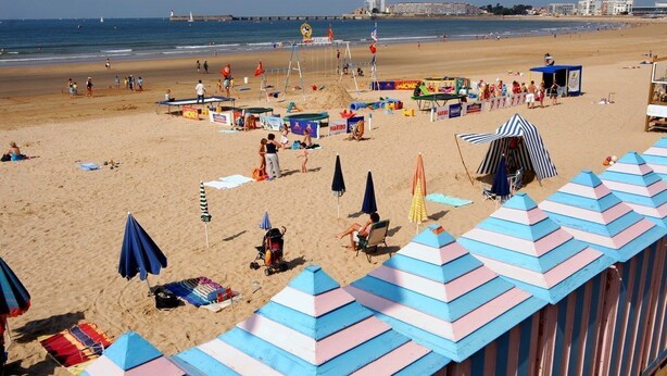 A beach with colorful umbrellas, beach chairs, and a lifeguard tower. - Proche du port | Balcon privé & vue sur le port (Les Sables d'Olonne)