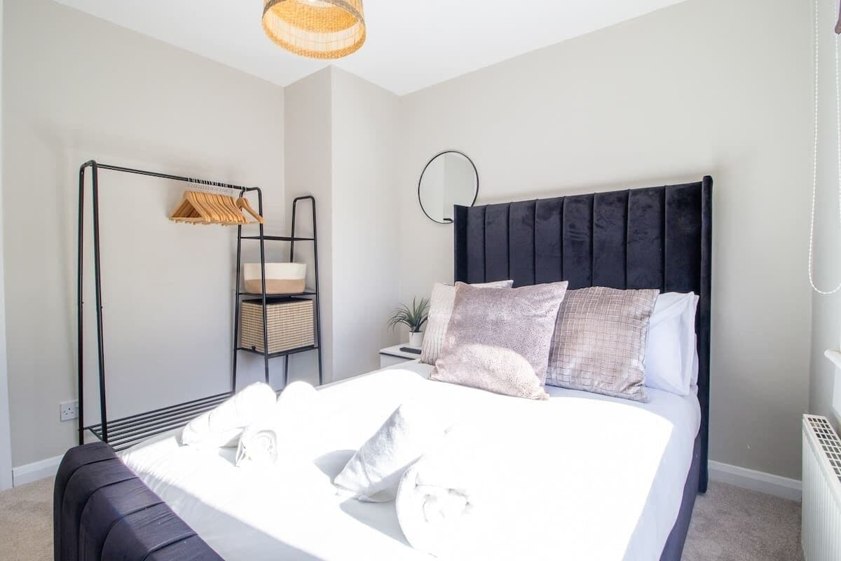 A neatly arranged bedroom with a bed, bedside tables, a hanging light fixture, and a wall-mounted shelf.