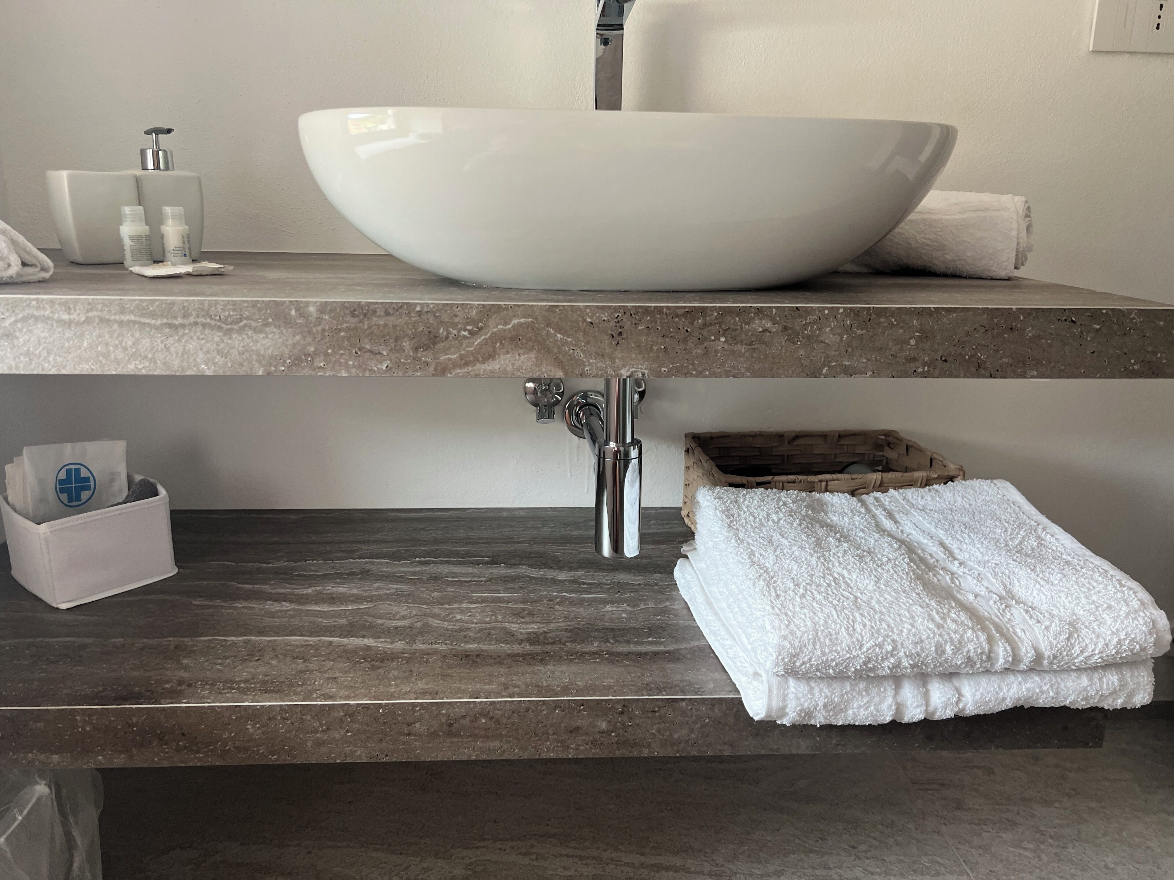 Ein Badezimmer mit einem großen, weißen Waschbecken, einem Wasserhahn, einer Seifenspender und einem Handtuch auf der Ablagefläche.