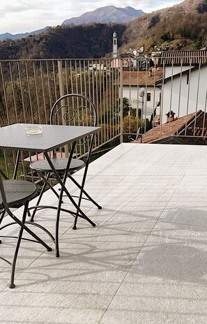 Eine Terrasse mit Tisch und Stühlen, einem Metallgeländer und Blick auf einen Berg sowie Gebäude.