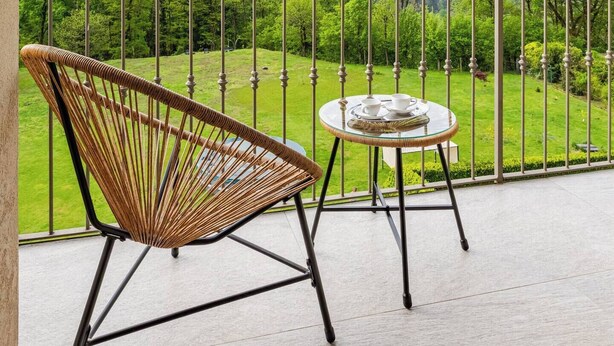 A balcony with a wicker chair and a small table, overlooking a green landscape and mountains. - Panoramic house 360° | 150sqm | 5 min from Lake Maggiore | Street parking (Cossogno)