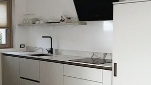 A modern kitchen with white cabinetry, a black countertop, and a flat-screen TV mounted above the sink. - Panoramic house 360° | 150sqm | 5 min from Lake Maggiore | Street parking (Cossogno)