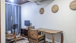 Une pièce comprenant un bureau en bois, une chaise, un téléviseur, un ventilateur et une décoration murale à motifs.