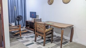 Une petite pièce avec une table en bois, deux chaises, un téléviseur et un ventilateur.
