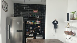 A kitchen with a black brick backsplash, stainless steel refrigerator, wooden table, and shelves with various kitchen items. - Studio 5 minutes from Copacabana and Ipanema beaches (Rio de Janeiro)