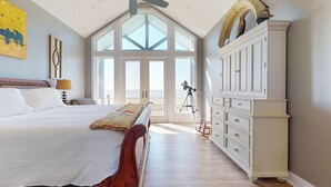 Ein Schlafzimmer mit einem großen Bett, einem Schminktisch, einem Teleskop und einem Balkon mit Blick.