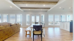 A spacious room with a wooden floor, a dining table with chairs, a sofa, and large windows offering a view. - Sea Time: 4 BR, 3 BA House in Crystal Beach, Sleeps 12 (Crystal Beach)