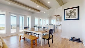 A spacious dining area with a wooden table and chairs, a bench, a ceiling fan, and a kitchen in the background. - Sea Time: 4 BR, 3 BA House in Crystal Beach, Sleeps 12 (Crystal Beach)