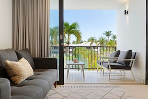 A modern living room with a sofa, a coffee table, and a balcony with a view of palm trees. - Luxe Yunque Retreat | Pool & Beach Access (Río Grande)