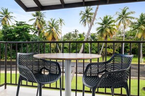 A balcony with a round table and two chairs, surrounded by a metal railing, overlooking a road with palm trees in the background. - Luxe Yunque Retreat | Pool & Beach Access (Río Grande)