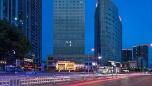 A modern hotel with a prominent sign, surrounded by high-rise buildings and a busy street at dusk. - Vienna International Hotel - Dayong city (Zhangjiajie)