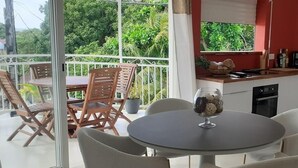 Un balcone con un tavolo e sedie, un angolo cottura con finestra, e vista su un verde lussureggiante.