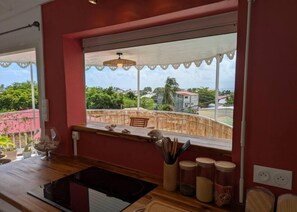 A kitchen with a window overlooking a fenced area, a wooden countertop, and a hanging light fixture. - Beautiful 3-star apartment-Sea view-Terrace-tank-5-minute range-Town center (Saint-François)