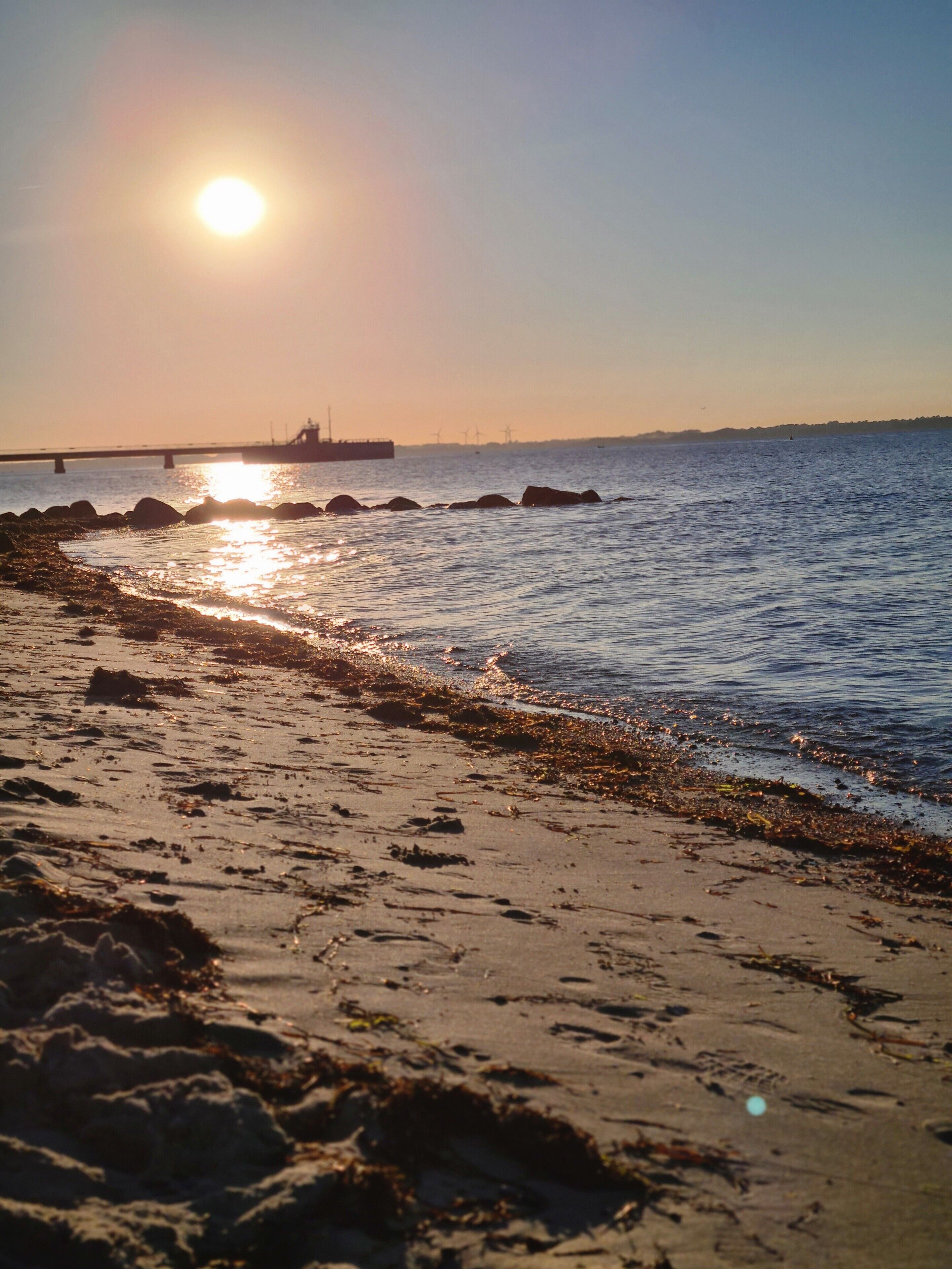Ein Strand mit Sonnenschein, der sich im Wasser, auf Felsen und Sand spiegelt.