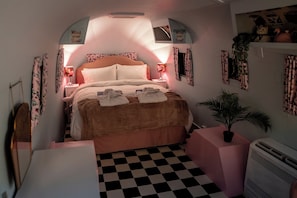 A bedroom with a checkered floor, a bed with pillows, a bedside lamp, a plant, and a wall-mounted heater. - Sleeps 2 - Hot Tub - Pet Friendly - Peggysue (Skegness)
