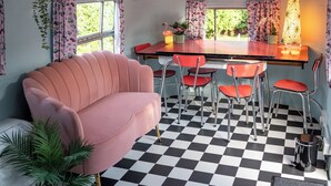 A room with a pink sofa, a checkered floor, a bar area with red chairs, and a window with curtains. - Sleeps 2 - Hot Tub - Pet Friendly - Peggysue (Skegness)