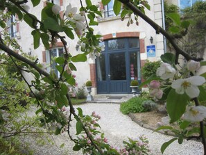 Un edificio con puerta azul, un camino de grava y árboles en flor.