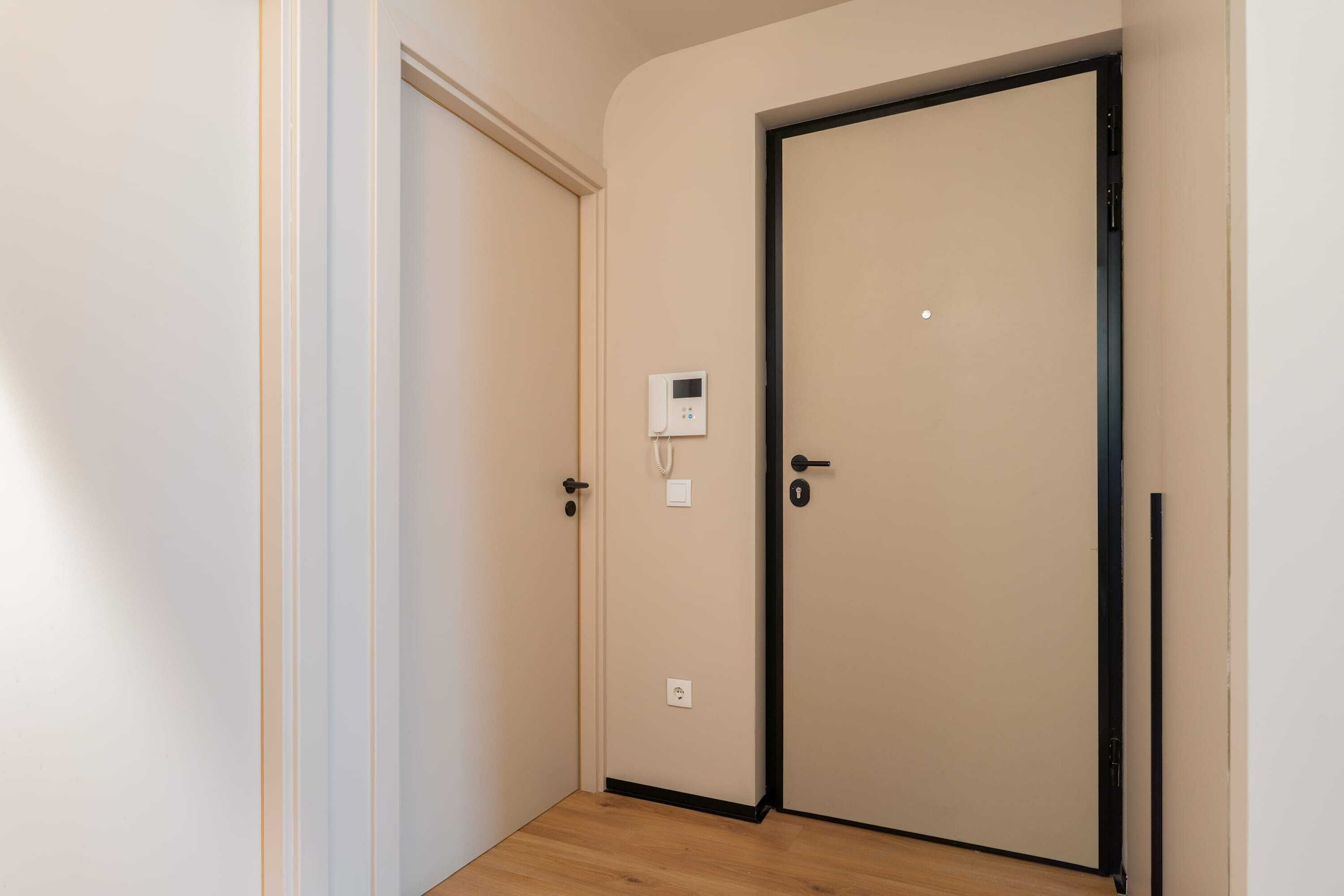 A hallway with a door on the right, a wall-mounted thermostat, and a light switch.