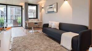 Un salon moderne avec un canapé foncé, un tapis blanc et un coin repas comprenant une table et des chaises.