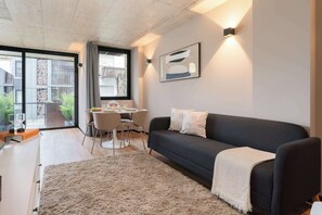 Ein modernes Wohnzimmer mit einem dunklen Sofa, einem weißen Teppich und einem Essbereich mit Tisch und Stühlen.