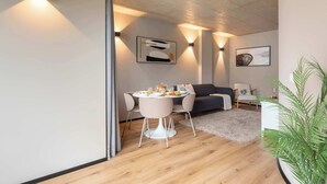 Un salon moderne avec un coin repas, doté d’un parquet, d’un canapé, d’une table à manger avec des chaises et d’un éclairage mural.