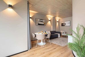 Ein modernes Wohnzimmer mit Essbereich, mit Holzboden, einer Couch, einem Esstisch mit Stühlen und Wandleuchten.