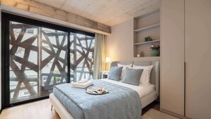Une chambre moderne avec un grand lit, une table de chevet, une lampe et une vue sur l’extérieur à travers une fenêtre ornée d’un motif géométrique.