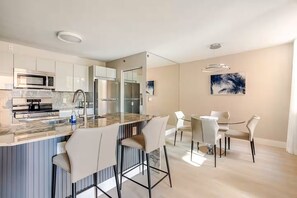 Eine moderne Küche mit Kochinsel, Edelstahlgeräten und einem Essbereich mit weißen Stühlen und einem Glastisch.