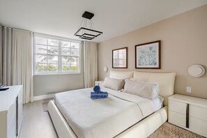 Ein Hotelzimmer mit einem großen Bett, einem Schreibtisch, einem Stuhl, einem Nachttisch und einem Fenster mit Vorhängen.