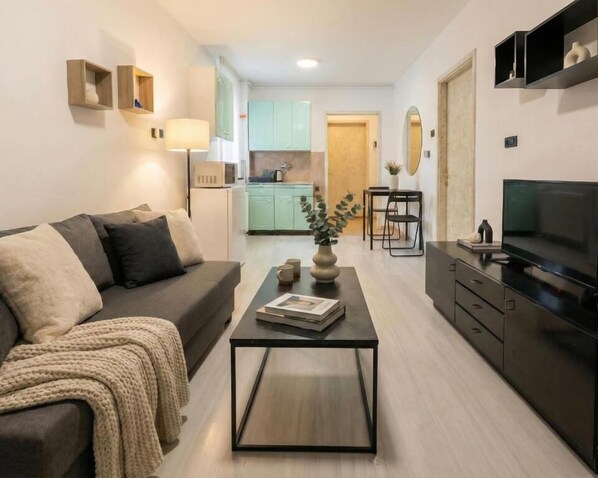 A modern living room with a sofa, coffee table, TV, and kitchen in the background.