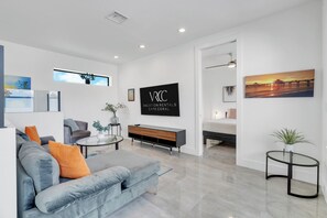 Un salon moderne avec un canapé gris, une table basse, un téléviseur et un lit à l’arrière-plan.