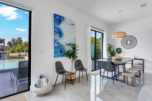 Un espace de restauration moderne avec vue sur une piscine, une grande peinture abstraite et une table à manger avec des chaises.
