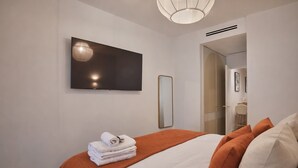 A hotel room with a bed, a flat-screen TV mounted on the wall, a mirror, and a door leading to a bathroom. - Beautiful Renovated Apartment With AC - Paris East (Paris)