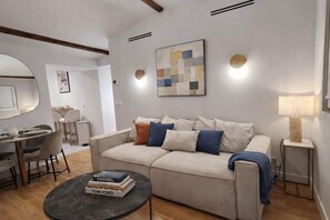 A modern living room with a sofa, a coffee table with books, a dining area with chairs, and a lamp. - Beautiful Renovated Apartment With AC - Paris East (Paris)