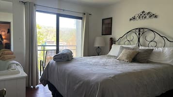 Un dormitorio con cama, mesita de noche, lámpara y vistas al exterior.
