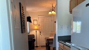 A kitchen with wooden cabinets, a white refrigerator, a dining table with chairs, a floor lamp, and a door with a framed picture. - Lovely Private Apartment with Pool in Walking Distance to Downtown Gatlinburg. (Gatlinburg)
