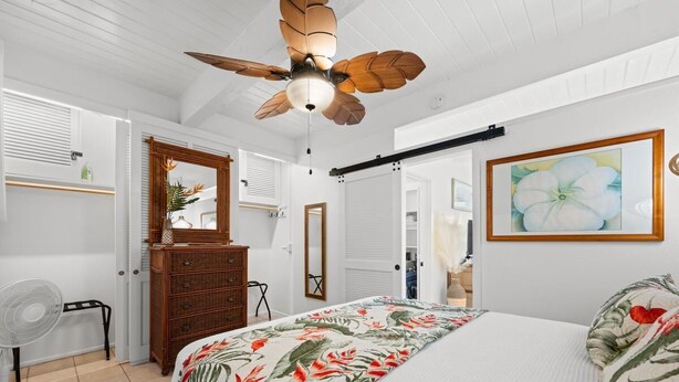 Ein Schlafzimmer mit einem Bett, einem Deckenventilator, einem Schminktisch, einem Spiegel und einem Bild an der Wand.