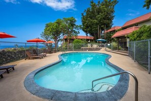 A swimming pool with lounge chairs and umbrellas, surrounded by a fence and trees. - Kona Mansions#b217 Beautiful Unit With Ocean View! (Kailua-Kona)