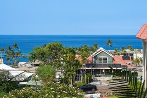 A coastal property with a view of the ocean, a green building with solar panels, and lush greenery. - Kona Mansions#b217 Beautiful Unit With Ocean View! (Kailua-Kona)