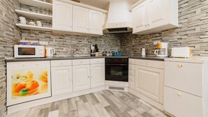 Una cocina con gabinetes blancos, microondas, estufa y cafetera.